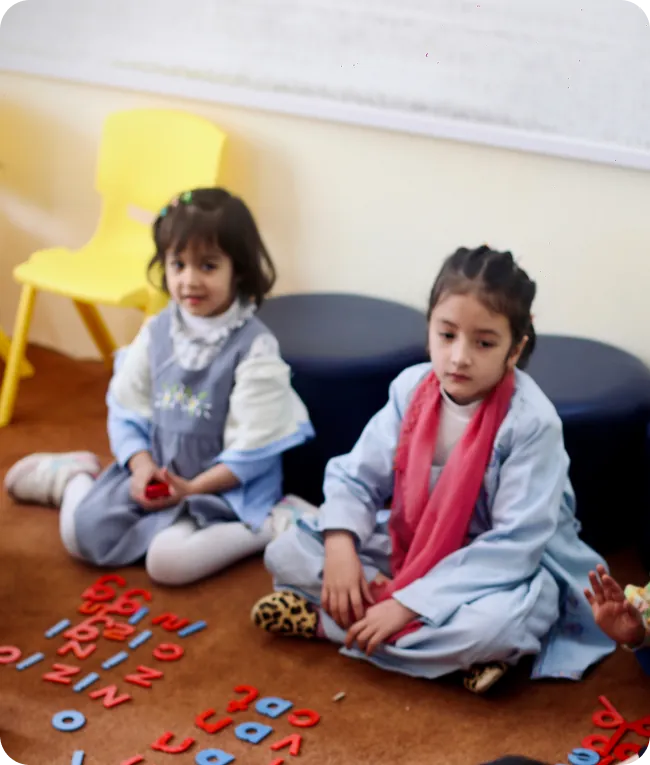 Two young students sitting on the floor playing with letter tiles
